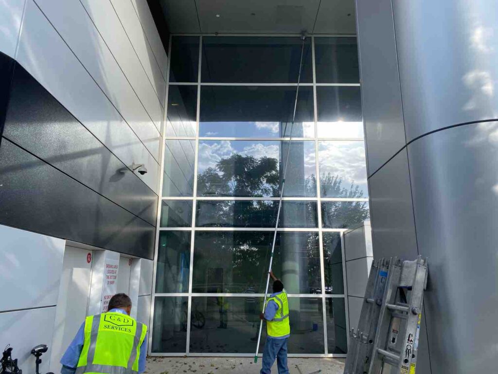 Two professional window cleaners from C & D Commercial Services in safety vests cleaning the large glass windows of a modern commercial building in the Dallas-Fort Worth area.